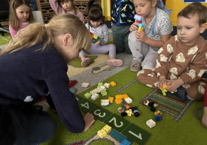 Dzieci siedzą na dywanie, bawią się klockami i poznają cyfrę 7.