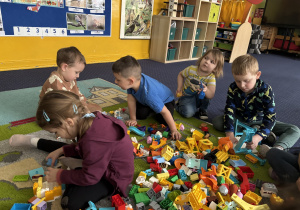 Dzieci siedzą na dywanie i bawią się klockami Lego duplo.