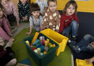 Dzieci siedzą na dywanie i bawią się klockami Lego duplo.