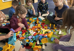 Dzieci siedzą na dywanie i bawią się klockami Lego duplo.