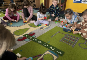Dzieci siedzą na dywanie i bawią się klockami Lego duplo oraz poznają cyfry.