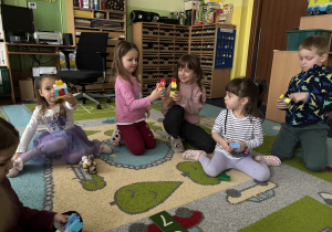 Dzieci siedzą na dywanie i bawią się klockami Lego duplo.