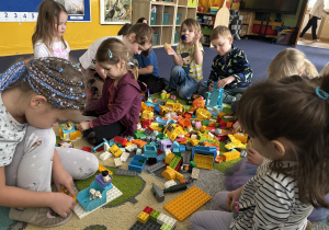 Dzieci siedzą na dywanie i bawią się klockami Lego duplo.