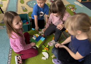 Dzieci siedzą na dywanie i bawią się klockami Lego duplo.
