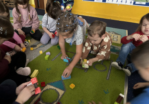 Dzieci siedzą na dywanie i bawią się klockami Lego duplo.