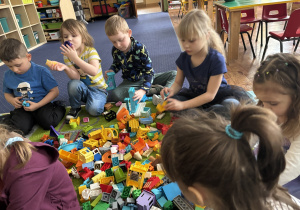 Dzieci siedzą na dywanie i bawią się klockami Lego duplo.
