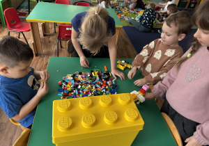 Dzieci są przy stoliku i bawią się klockami Lego.