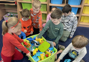 Dzieci siedzą na dywanie i budują z klocków Lego.