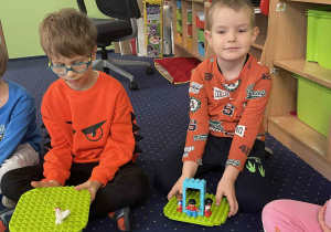 Dzieci siedzą na dywanie i budują z klocków Lego.