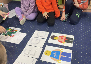 Dzieci siedzą na dywanie i słuchają pani.