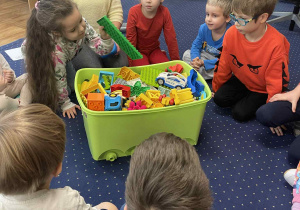 Dzieci siedzą na dywanie i budują z klocków Lego.