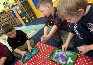 Dzieci siedzą na dywanie i badają kolorowy śnieg.