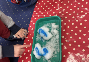 Dzieci siedzą na dywanie i badają kolorowy śnieg.