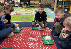 Dzieci siedzą na dywanie i badają śnieg.