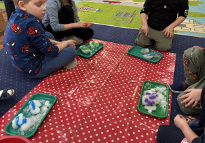 Dzieci siedzą na dywanie i badają kolorowy śnieg.