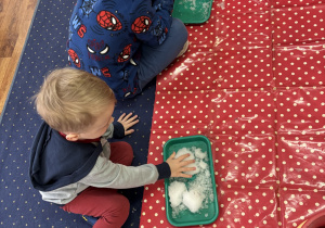 Dzieci siedzą na dywanie i badają śnieg.