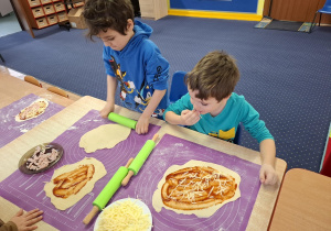 dzieci samodzielnie przy stolikach przygotowują pizzę