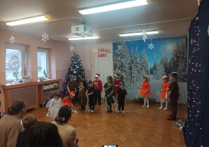 świateczny występ dzieci na sali gimnastycznej. dzieci mówią wiersze, śpiewają piosenki, rodzice oglądają występ.