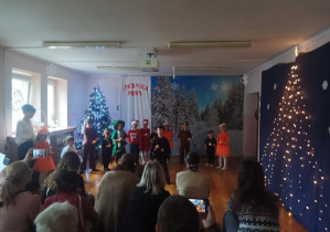 świateczny występ dzieci na sali gimnastycznej. dzieci mówią wiersze, śpiewają piosenki, rodzice oglądają występ.