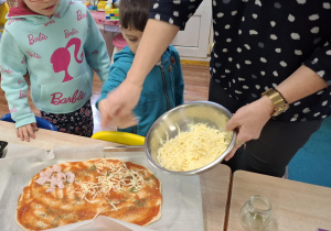 dzieci przy stolikach przygotowują pizzę