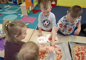 dzieci przy stolikach przygotowują pizzę