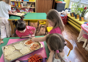 Dzieci siedzą przy stolikach i przygotowują własną pizzę.