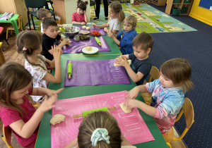 Dzieci siedzą przy stolikach i przygotowują własną pizzę.