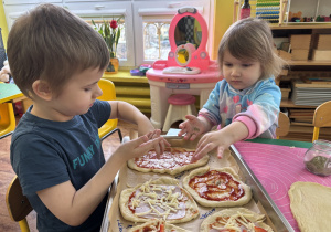 Dzieci siedzą przy stolikach i przygotowują własną pizzę.
