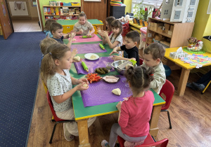 Dzieci siedzą przy stolikach i zjadają pizzę.
