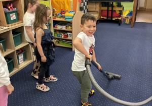 Chłopiec pokazuje jak wygląda praca z odkurzaczem.