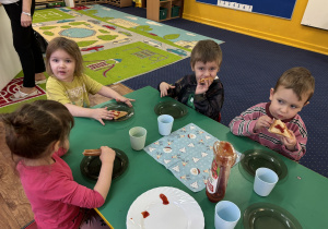 Dzieci siedzą przy stole i zjadają tosty.