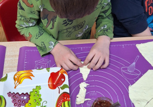 Chłopiec przy stole zwija rogaliki.