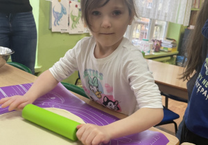 Przy stole dziewczynka wałkuje ciasto.