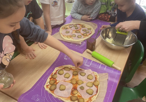 Przy stole dzieci układają produkty na pizzy.