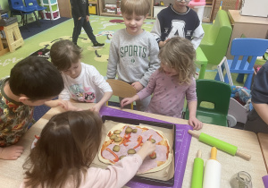 Przy stole dzieci układają produkty na pizzy.
