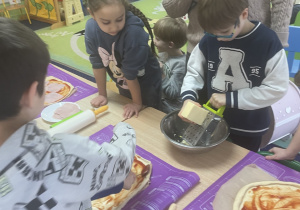 Przy stole chłopiec ściera ser.