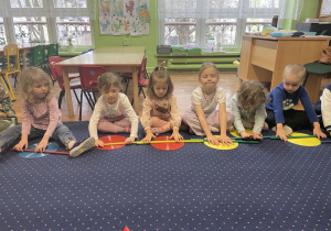 Dzieci siedzą na dywanie i uczą się wałkować ciasto.