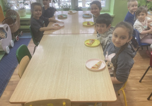 Dzieci siedzą przy stole na którym jest upieczona pizza.