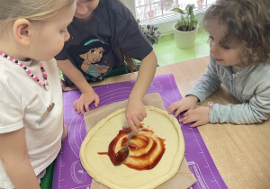 Przy stole dziewczynka nakłada sos na pizzę.