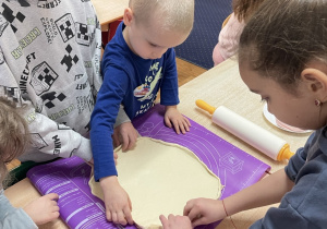 Przy stole dzieci formują ciasto na pizzę.