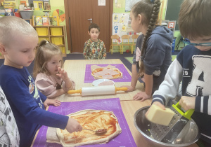 Przy stole dzieci przygotowują pizzę.
