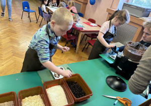 Chłopiec wkłada do czekolady dodatki, a dziewczynka wypełnia formy masą czekoladową.