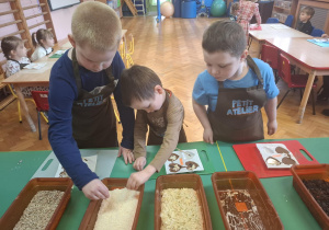 dzieci ubrane w brązowe fartuszki biorą udział w czekoladowych warsztatach, samodzielnie ozdabiają czekoladę w kształcie serca