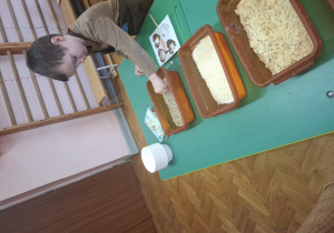 dzieci ubrane w brązowe fartuszki biorą udział w czekoladowych warsztatach, samodzielnie ozdabiają czekoladę w kształcie serca