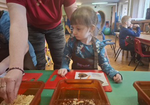 dzieci ubrane w brązowe fartuszki biorą udział w czekoladowych warsztatach, samodzielnie ozdabiają czekoladę w kształcie serca