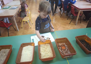 dzieci ubrane w brązowe fartuszki biorą udział w czekoladowych warsztatach, samodzielnie ozdabiają czekoladę w kształcie serca