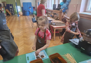 dzieci ubrane w brązowe fartuszki biorą udział w czekoladowych warsztatach, samodzielnie ozdabiają czekoladę w kształcie serca