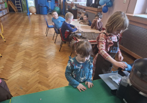 dzieci ubrane w brązowe fartuszki biorą udział w czekoladowych warsztatach, samodzielnie ozdabiają czekoladę w kształcie serca