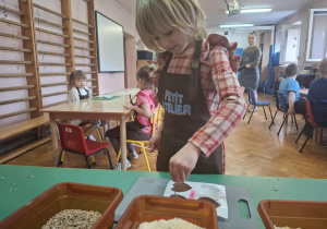 dzieci ubrane w brązowe fartuszki biorą udział w czekoladowych warsztatach, samodzielnie ozdabiają czekoladę w kształcie serca