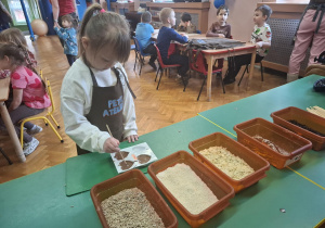 dzieci ubrane w brązowe fartuszki biorą udział w czekoladowych warsztatach, samodzielnie ozdabiają czekoladę w kształcie serca
